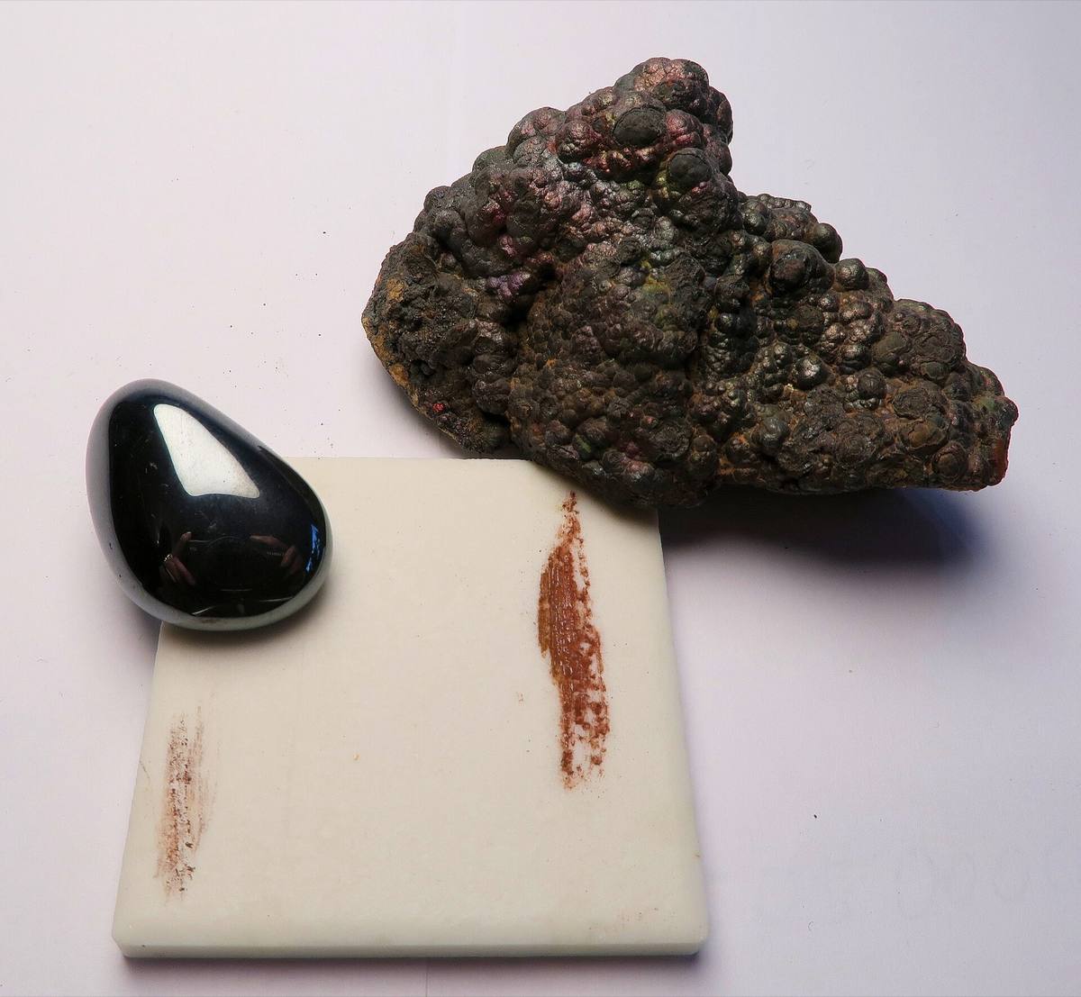 Hematite specimens beside their red-brown streak on a porcelain plate