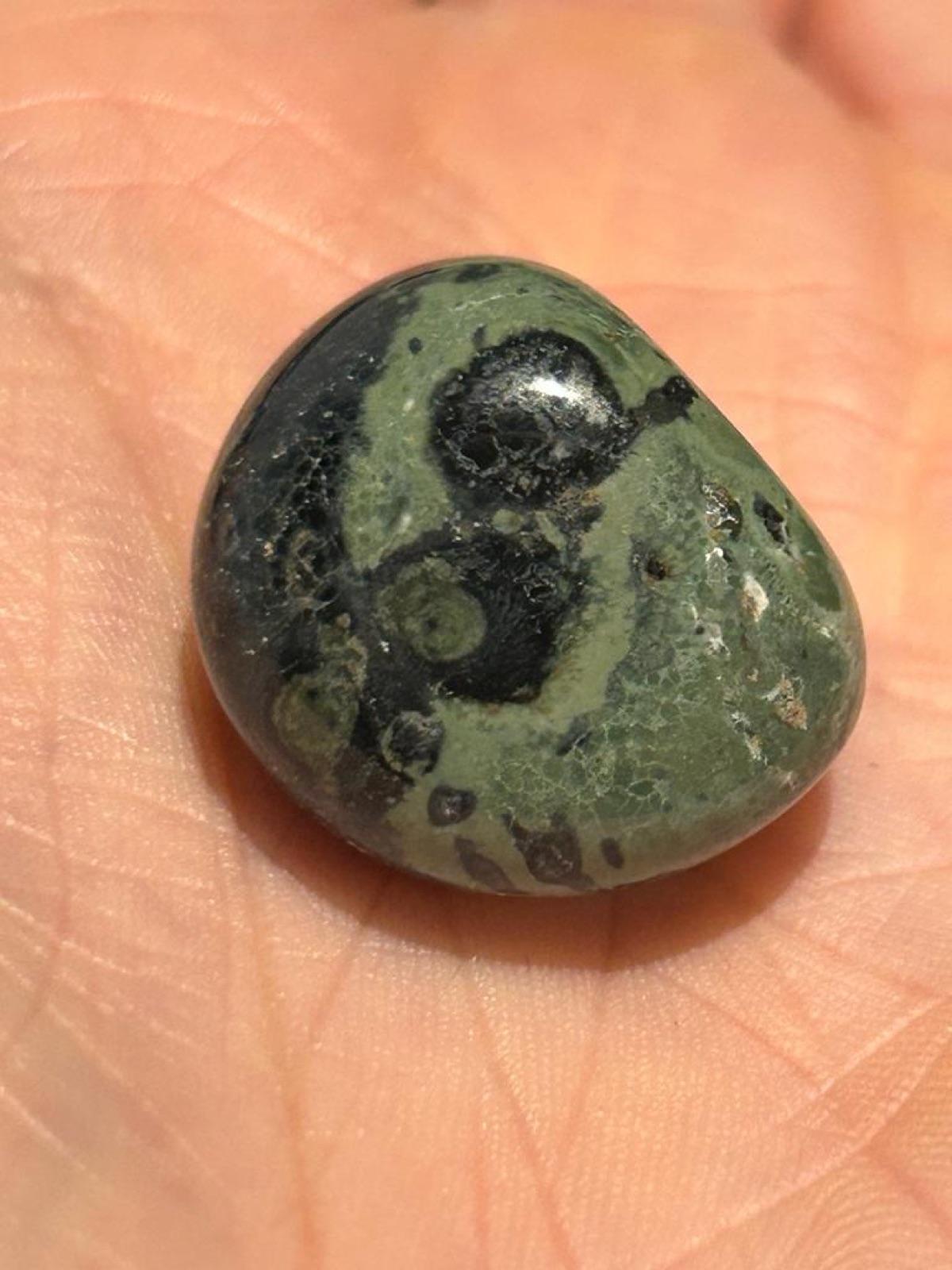 Tumbled kambaba jasper with black orbs on green, held in the hand