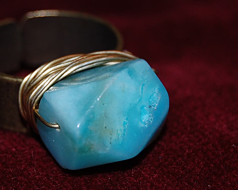 Opaque teal-blue Peruvian opal nugget, close view of the stone in a wire-wrapped ring
