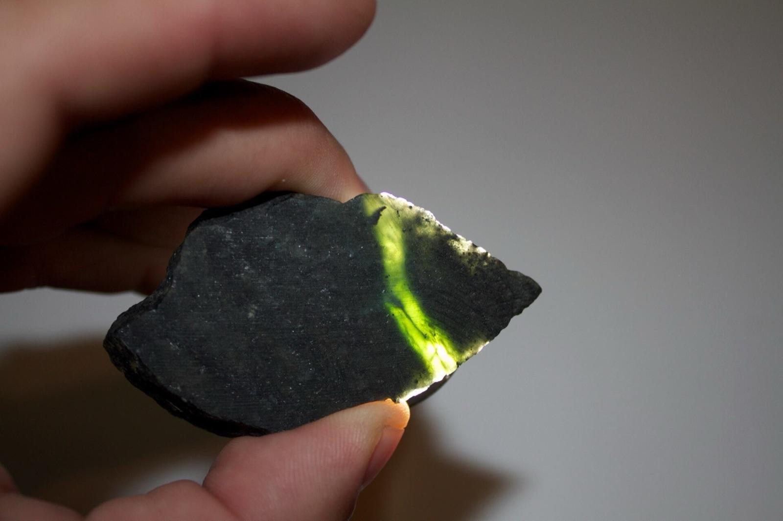 Dark serpentine glowing green at a thin edge held to the light